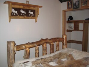 A wooden bed frame with carved details, a fur throw, and a wall-mounted shelf with moose carvings.