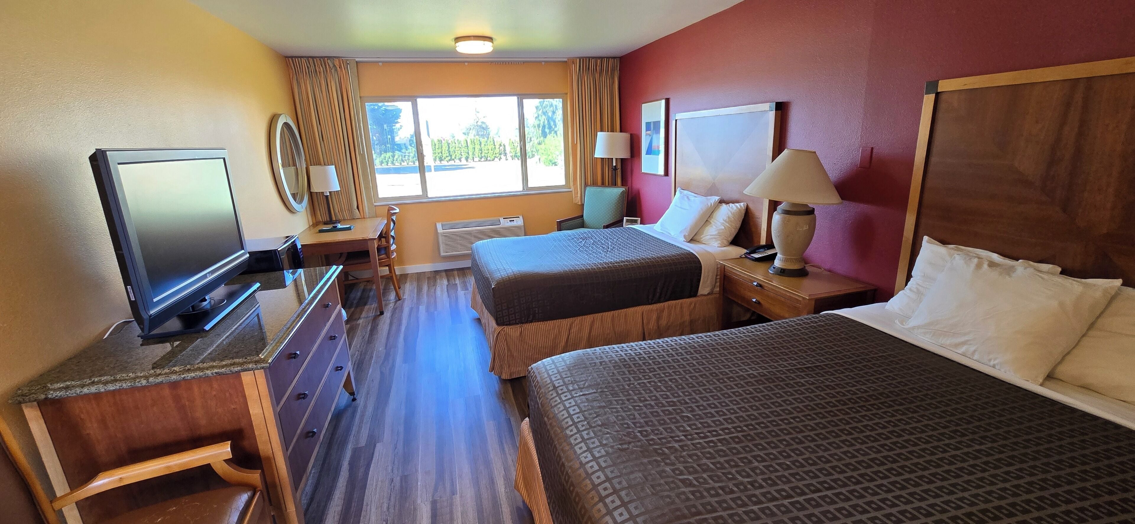 Une chambre d’hôtel avec deux lits, un bureau avec une télévision, une chaise et une fenêtre avec des rideaux.