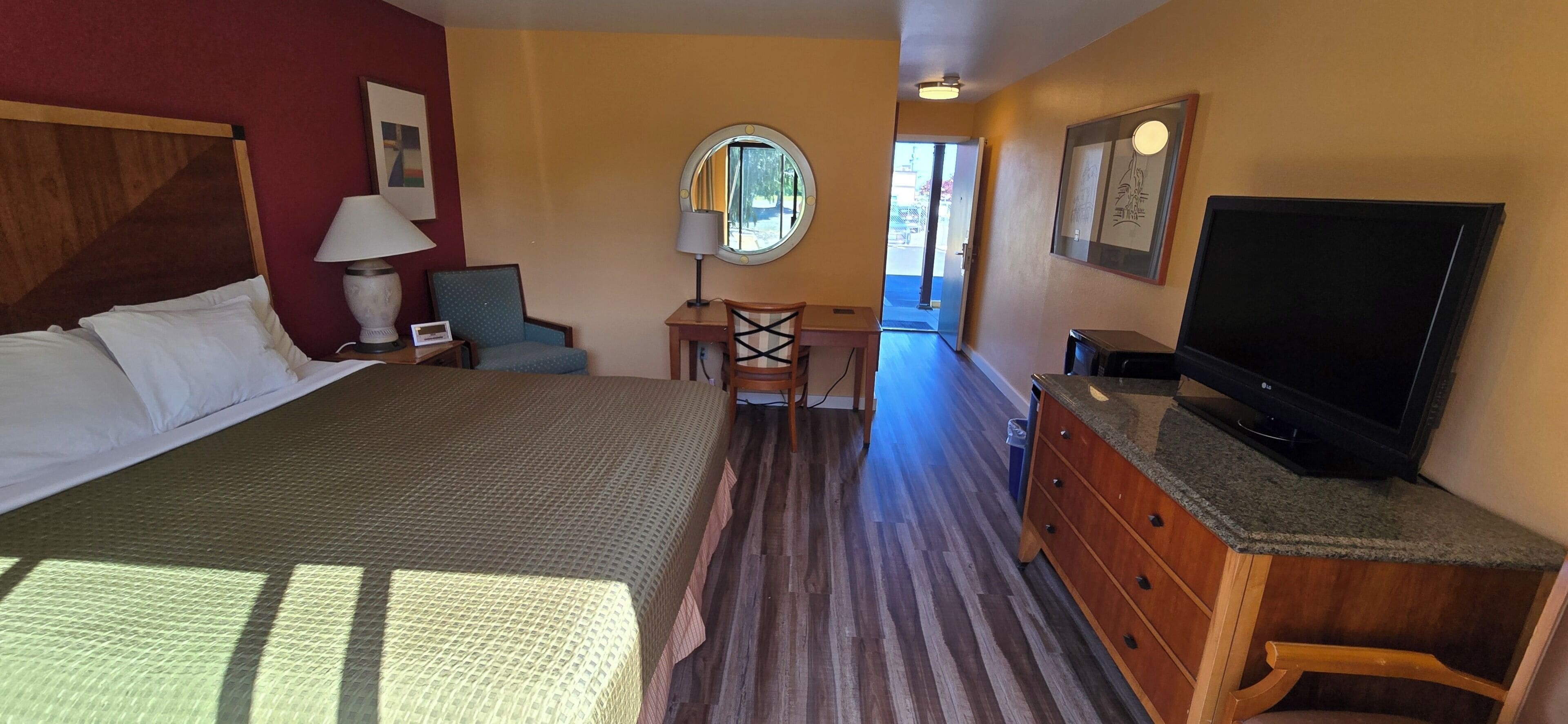 A hotel room with a bed, a desk, a chair, a television, and a window.