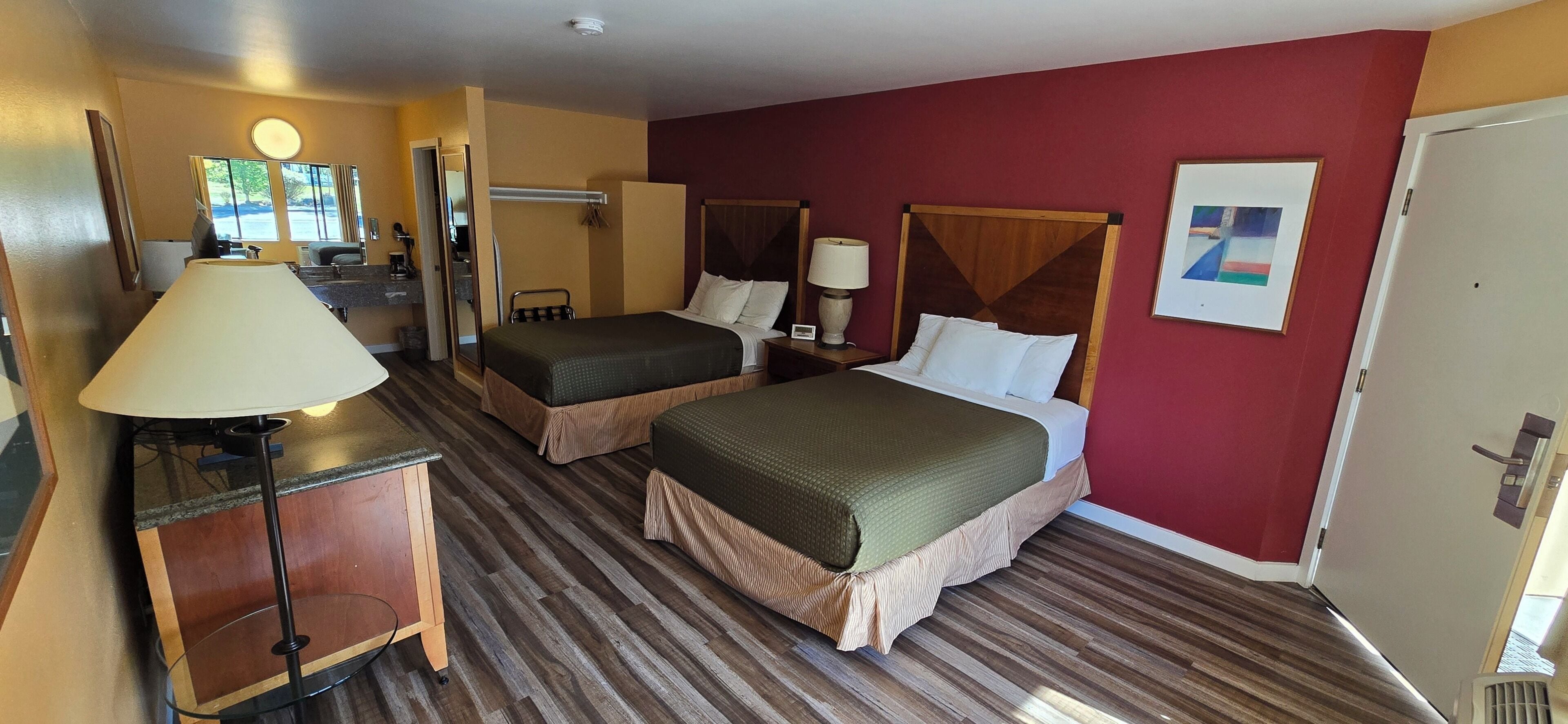 Ein Hotelzimmer mit zwei Betten, einem Schreibtisch mit Lampe, einem Stuhl, einem Fenster mit Aussicht und einer Tür.