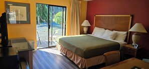 A hotel room with a bed, two bedside lamps, a desk with a computer, and a sliding glass door leading to an outdoor area. - Olympic View Inn (Sequim)