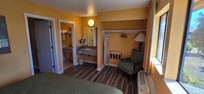 A hotel room with a bed, a bathroom with a shower, a chair, and a window with a view. - Olympic View Inn (Sequim)