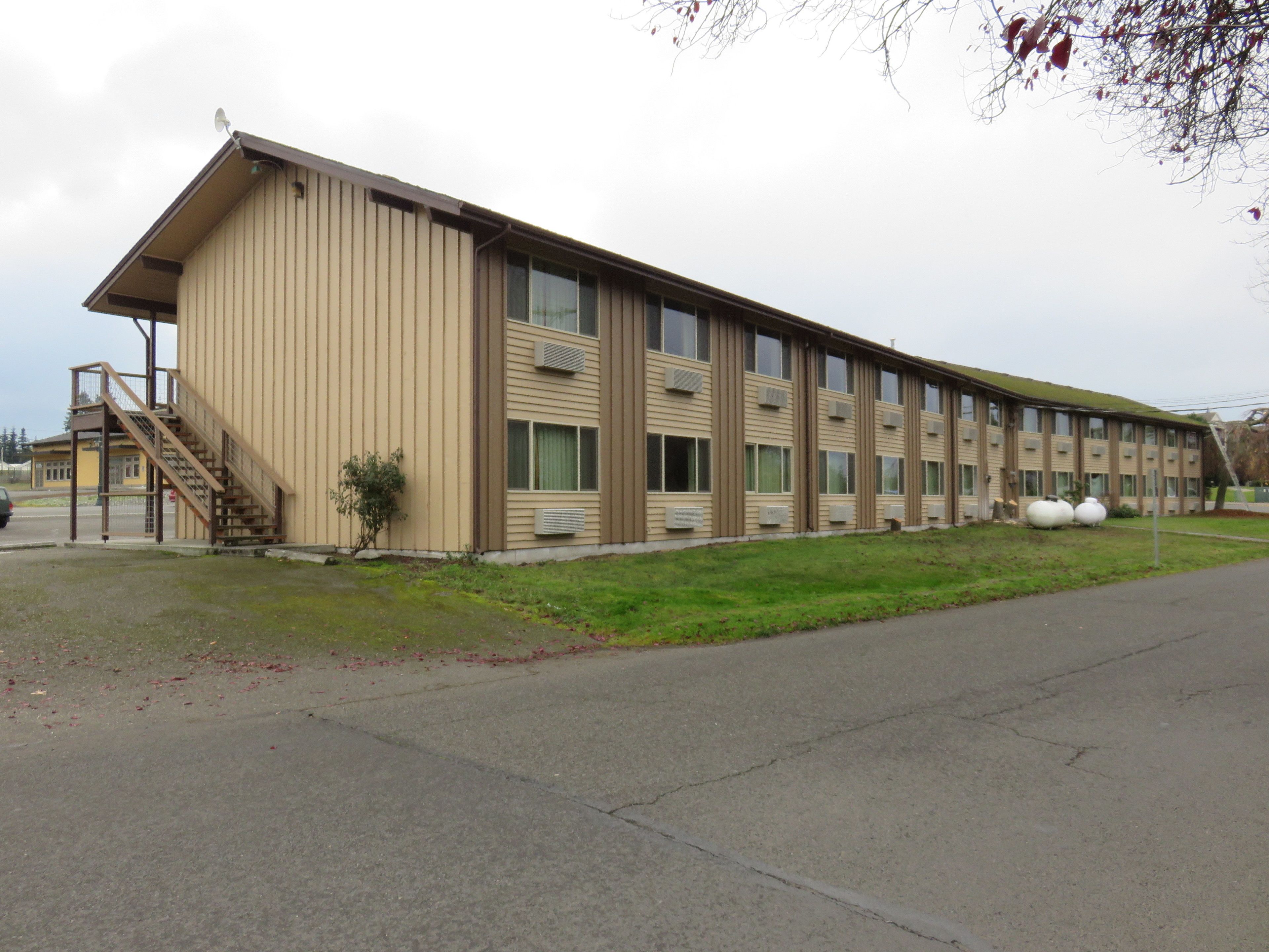 A long, single-story building with a beige exterior, multiple windows, and a staircase leading to an entrance.
