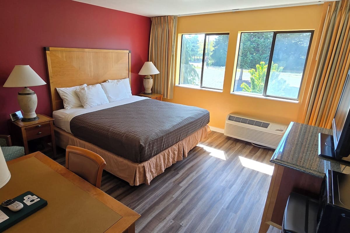 Quarto de hotel com cama, duas luminárias de cabeceira, escrivaninha com computador, televisão e janela com cortinas.