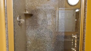 Un box de ducha con paredes de vidrio, piso de granito, ducha de mano y una toalla colgada en la pared.
