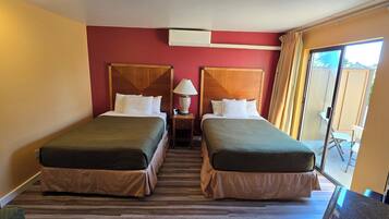 A hotel room with two beds, a nightstand, a lamp, and a sliding door to a balcony.