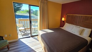 Una habitación de hotel con cama, mesita de noche, lámpara, silla y vistas a un balcón.