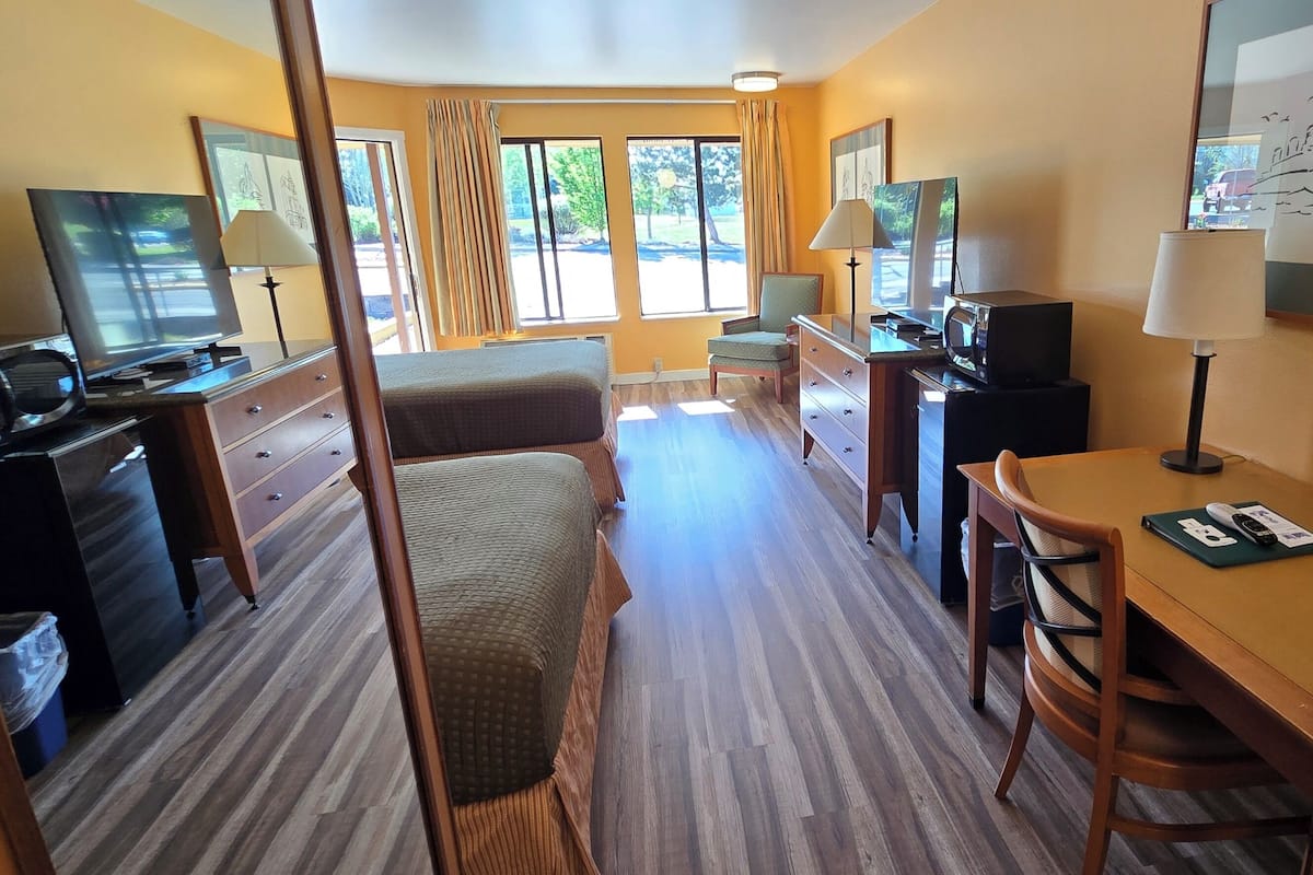 Quarto de hotel com cama, escrivaninha, cadeira, televisão e telefone.