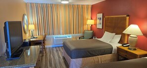 A hotel room with a bed, bedside table, lamp, TV, and curtains. - Olympic View Inn (Sequim)