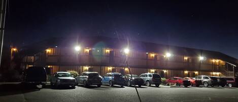 Un parcheggio con diverse auto parcheggiate di fronte a un edificio con numerose finestre illuminate.