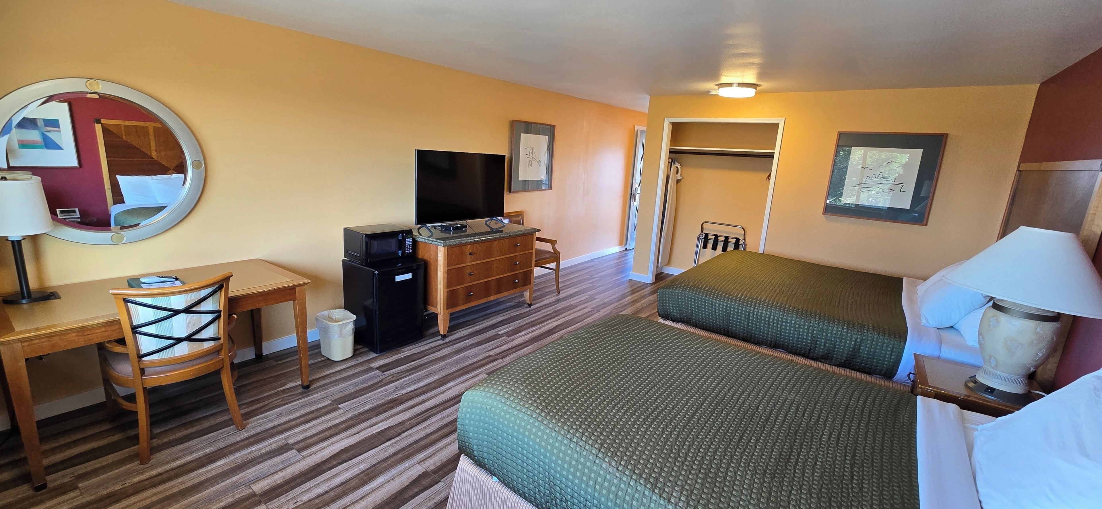 Ein Hotelzimmer mit Bett, Schreibtisch mit Stuhl, Fernseher, Mikrowelle, Kleiderschrank und Spiegel.