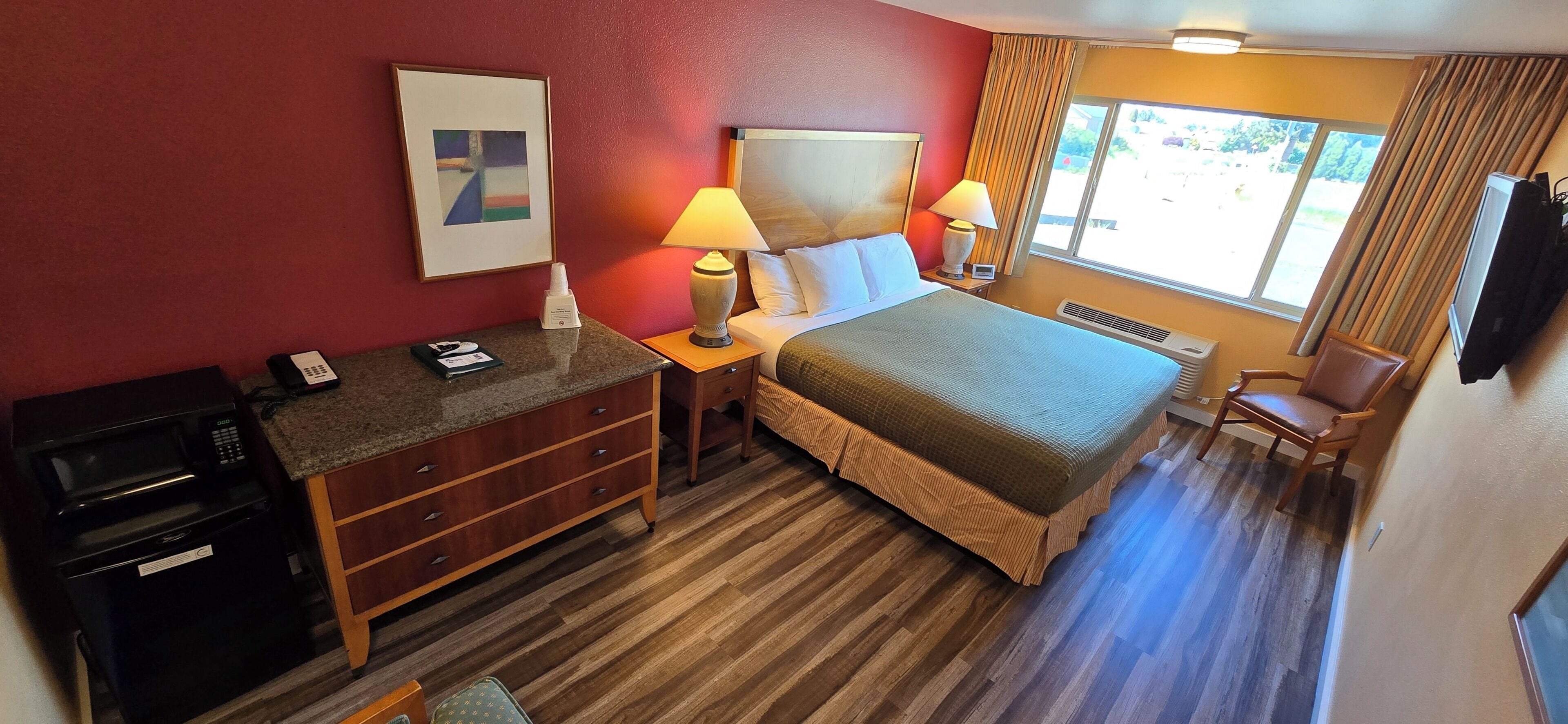 A hotel room with a bed, bedside lamps, a desk with a telephone, a microwave, and a television.