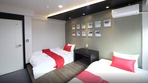 Een hotelkamer met twee bedden, een donker hoofdeinde, een wandairconditioner en ingekaderde foto's aan de muur.
