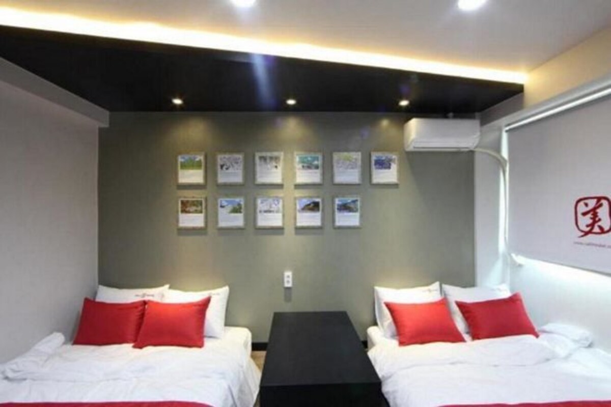 Ein Hotelzimmer mit zwei Betten, einem kleinen Tisch und einer Wand mit gerahmten Bildern.