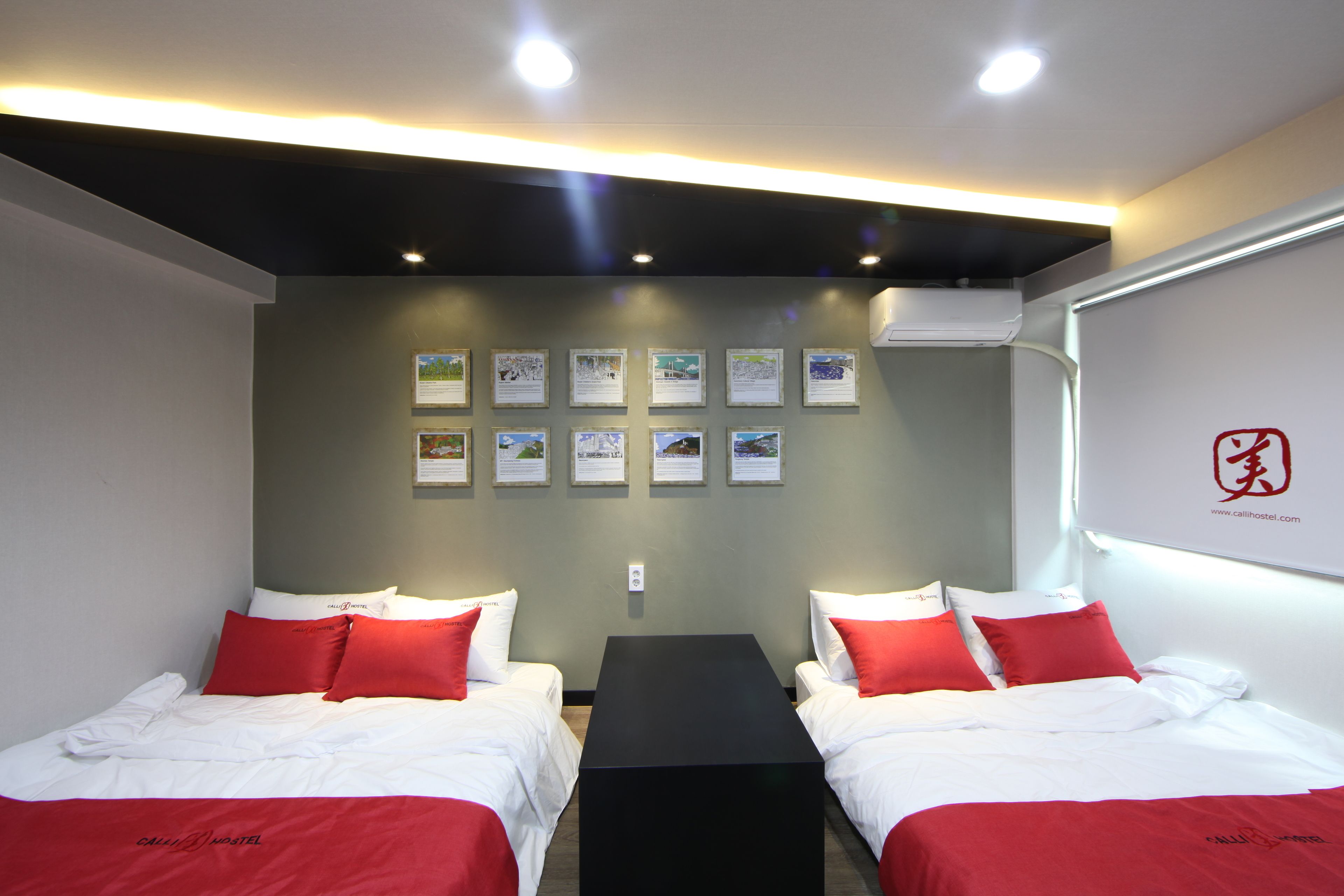 A hotel room with two beds, a black table, and a wall with framed informational posters.