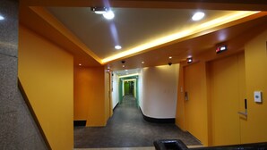 Een hal met een modern ontwerp, met gele en witte wanden, een grijze vloer en een plafond met inbouwverlichting.