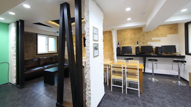 Een modern interieur met een donkergrijze vloer, een houten eethoek met tafel en stoelen, een zwarte bank en een keuken met houten details en twee zwarte monitoren.