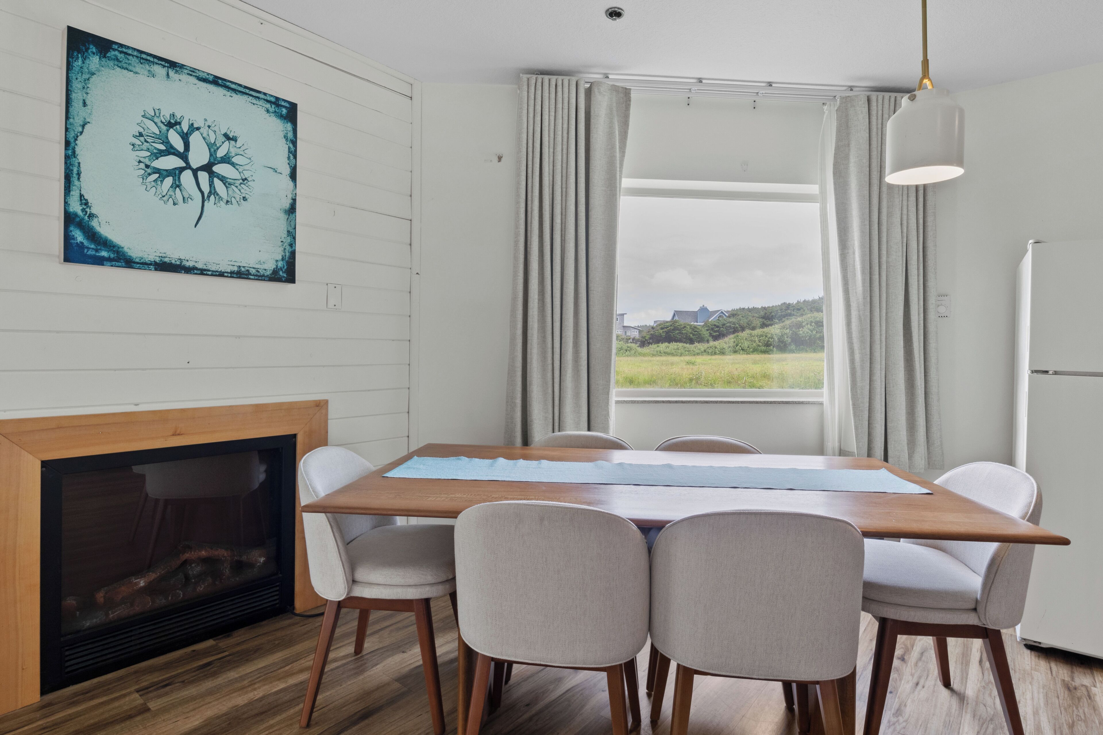 Un comedor con una mesa de madera, seis sillas, una chimenea y un ventanal con cortinas.
