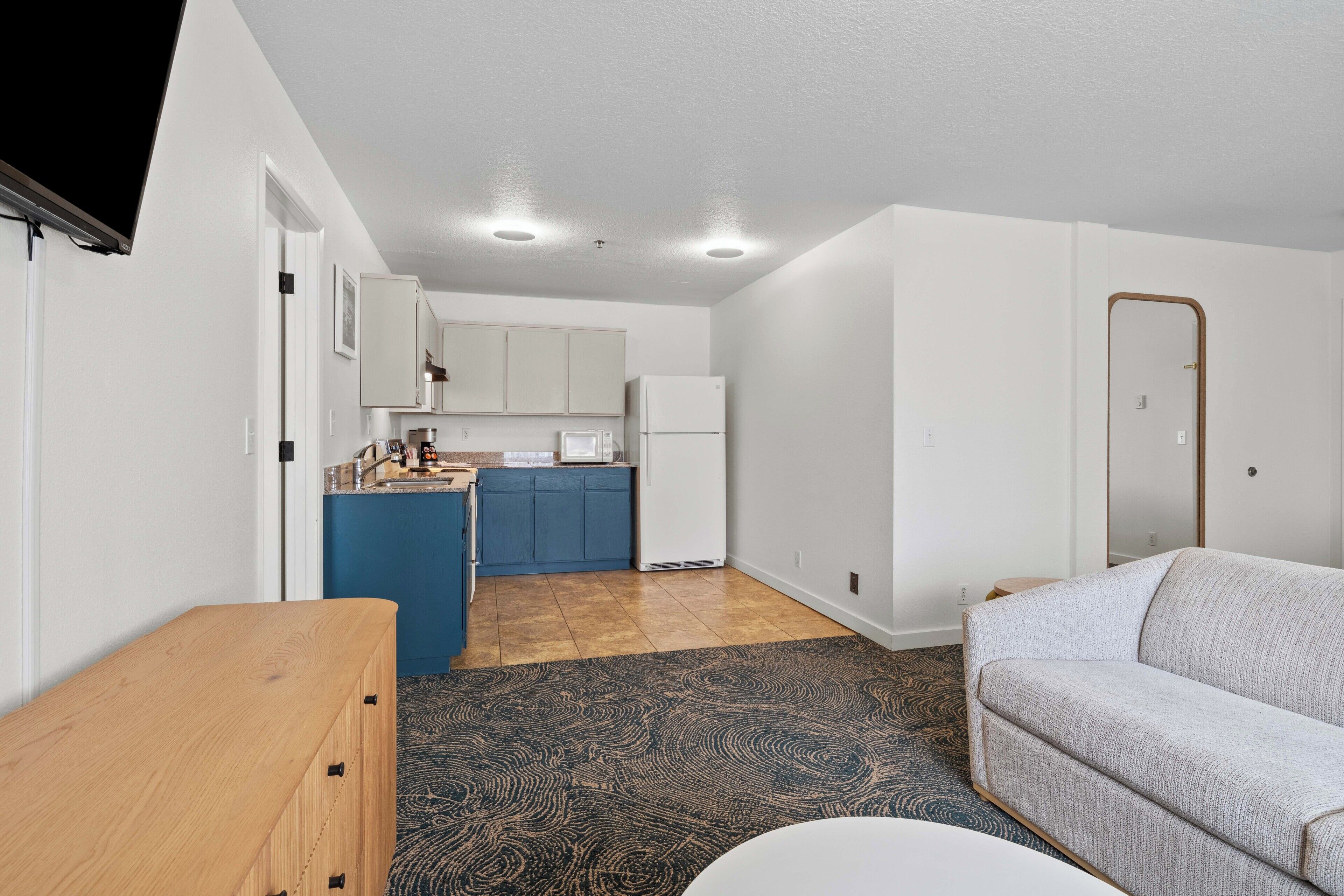 A compact living space with a kitchenette, a sofa, and a wooden table.