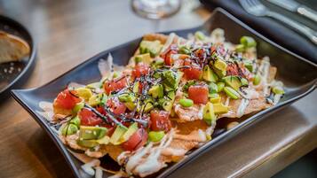 Un plato rectangular con nachos cubiertos de aguacate, tomates, guisantes verdes y una salsa cremosa.