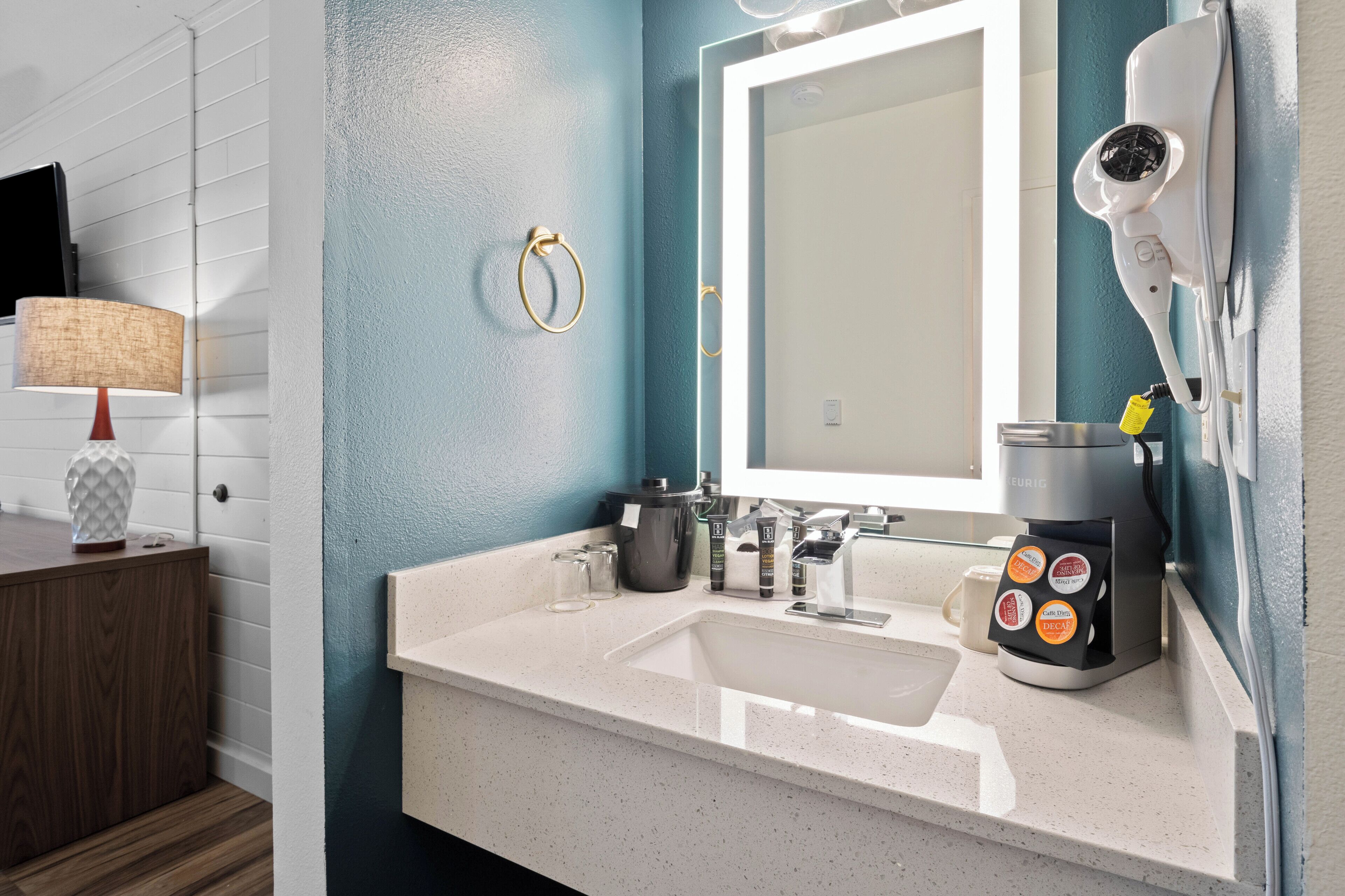 A modern bathroom with a white sink, a mirror, a hairdryer, and a coffee maker.