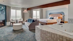 A hotel room with a large bed, a sitting area with a sofa and chairs, a small round table, a bathtub, and a view of the sea. - Adobe Resort (Yachats)