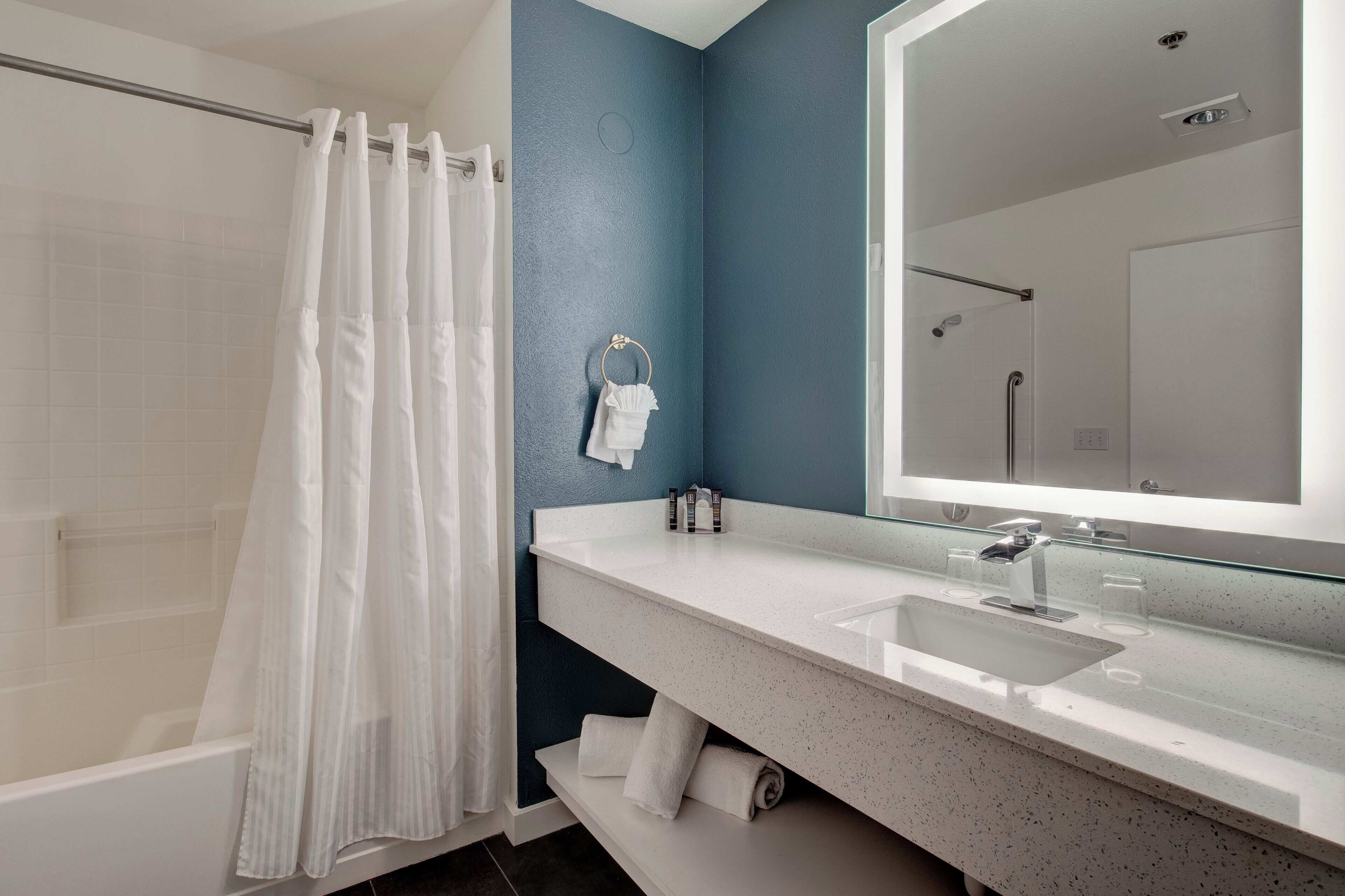 A modern bathroom with a white bathtub, a glass shower enclosure, a white sink with a large mirror, and a blue accent wall.