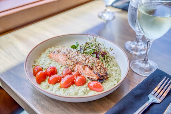 A plate of salmon with cherry tomatoes and greens, accompanied by a glass of white wine on a wooden table.