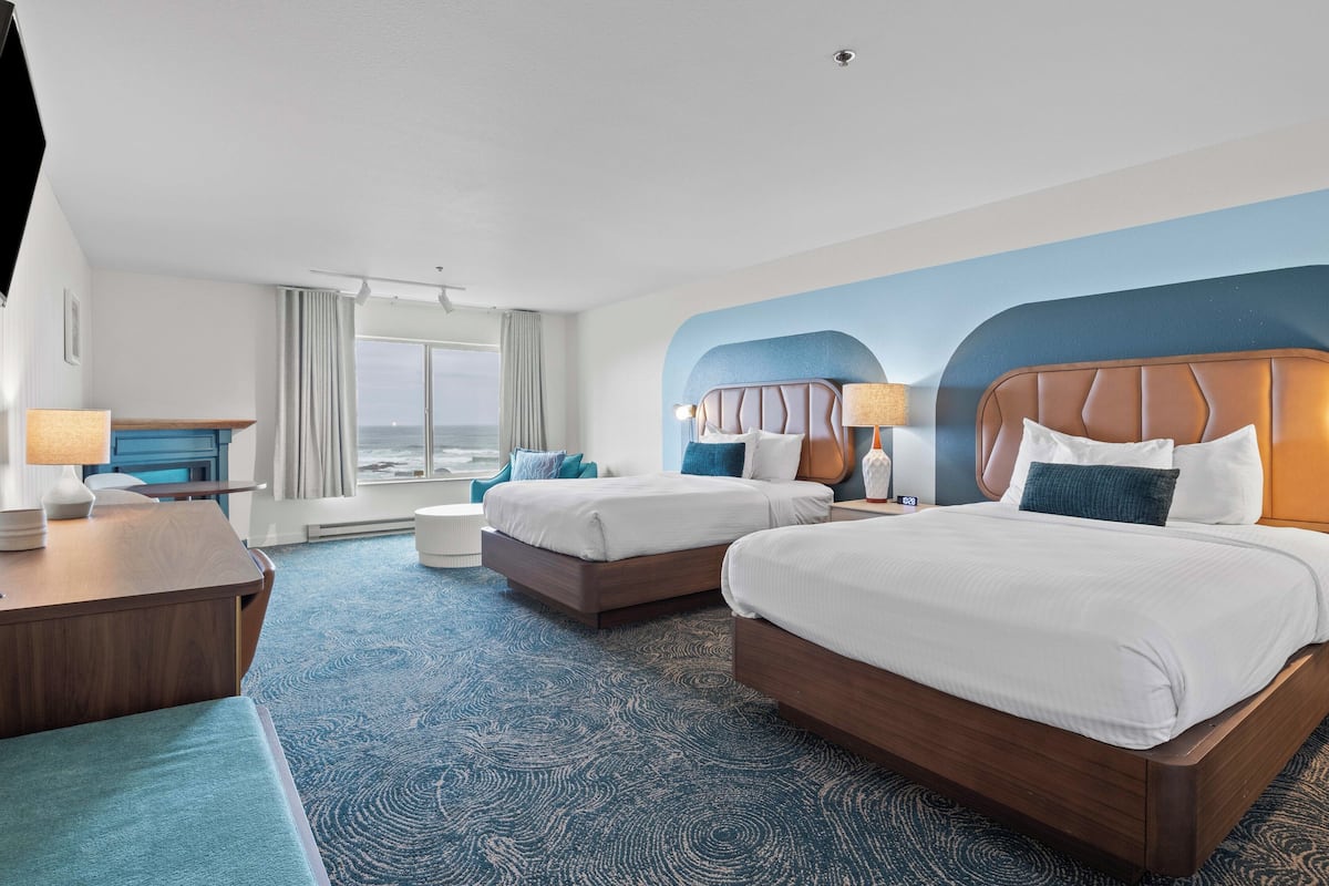 A hotel room with two beds, a desk, and a view of the ocean.