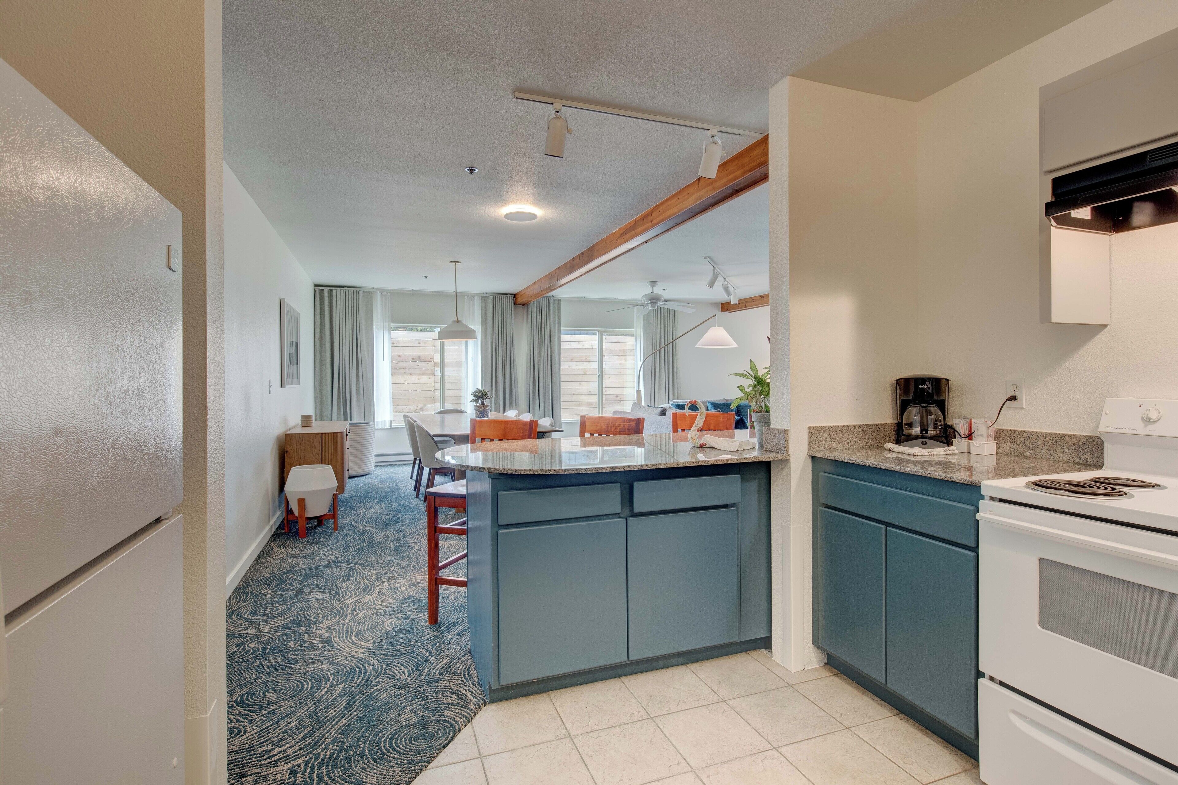 A compact kitchen with a central island, a dining area with chairs, and a view of the outdoors through large windows.