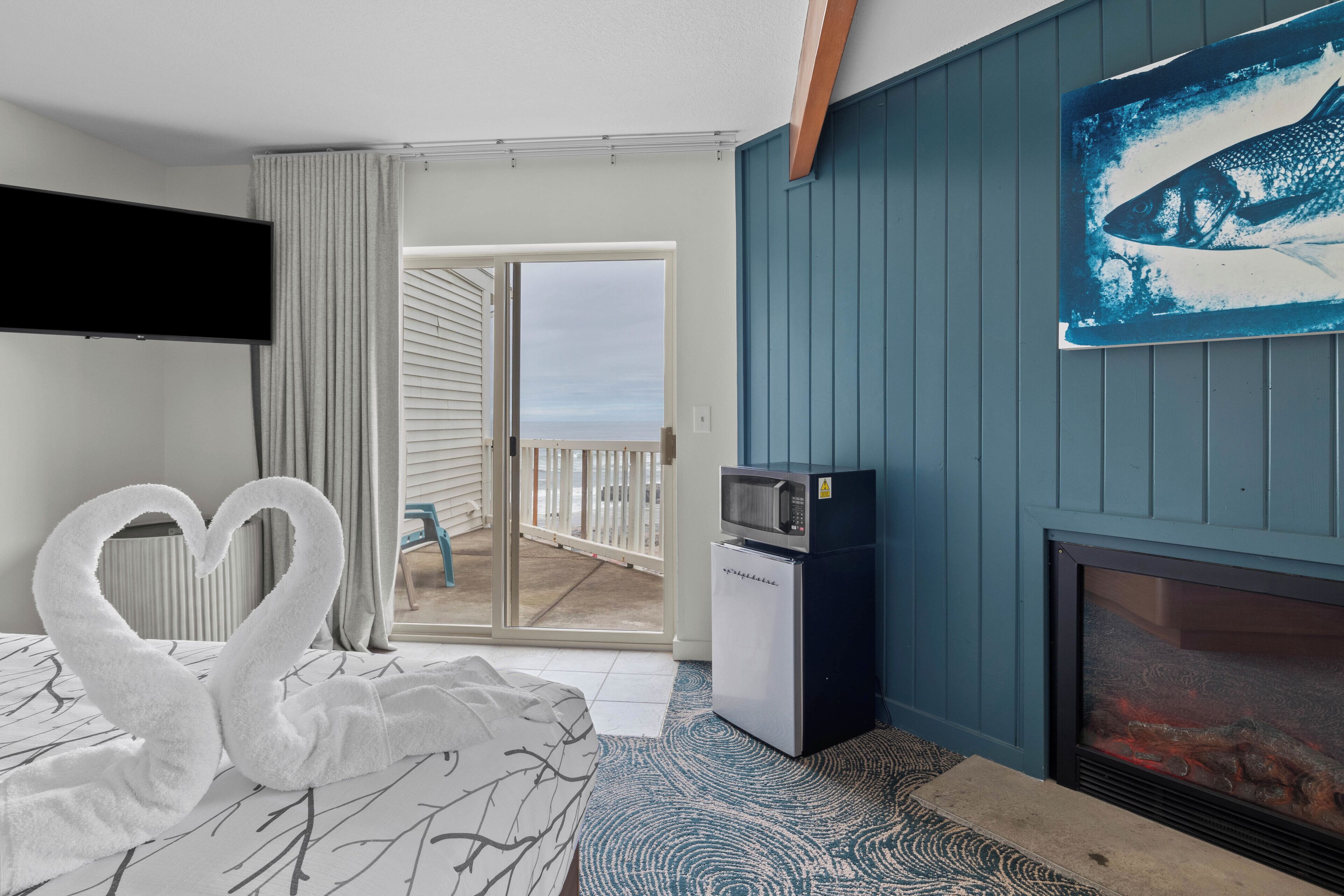 A hotel room with a bed, a flat-screen TV, a microwave, a fireplace, and a balcony with a view.