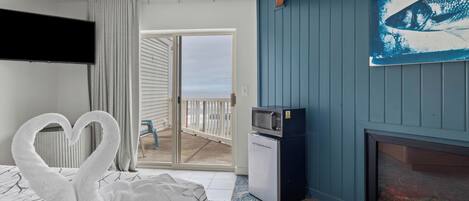 A hotel room with a bed, a flat-screen TV, a microwave, a fireplace, and a balcony with a view.