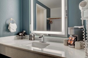 Un baño moderno con un espejo grande, un lavabo, un secador de pelo y una cafetera.