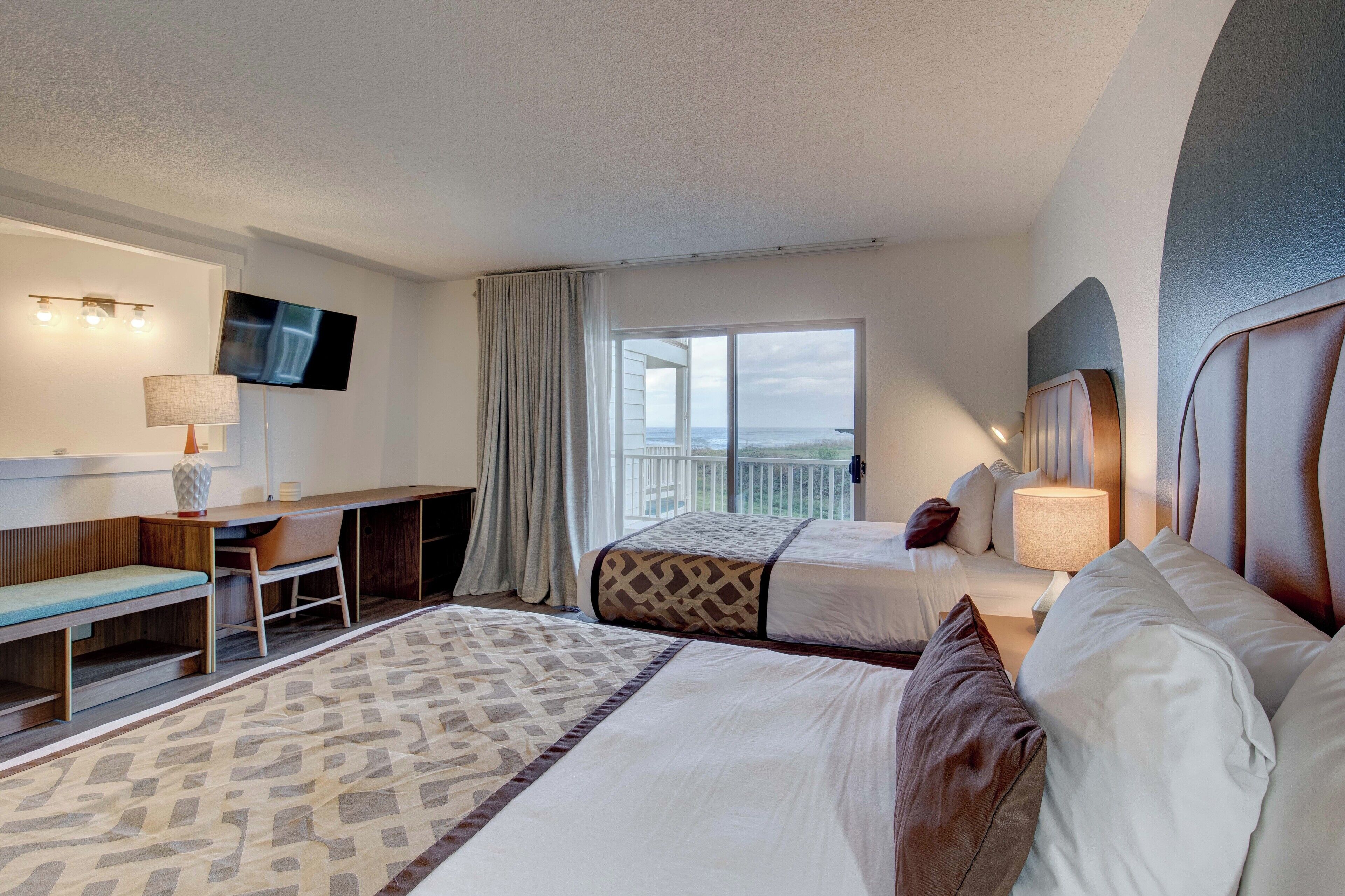 A hotel room with two beds, a desk, a TV, and a balcony with a view.