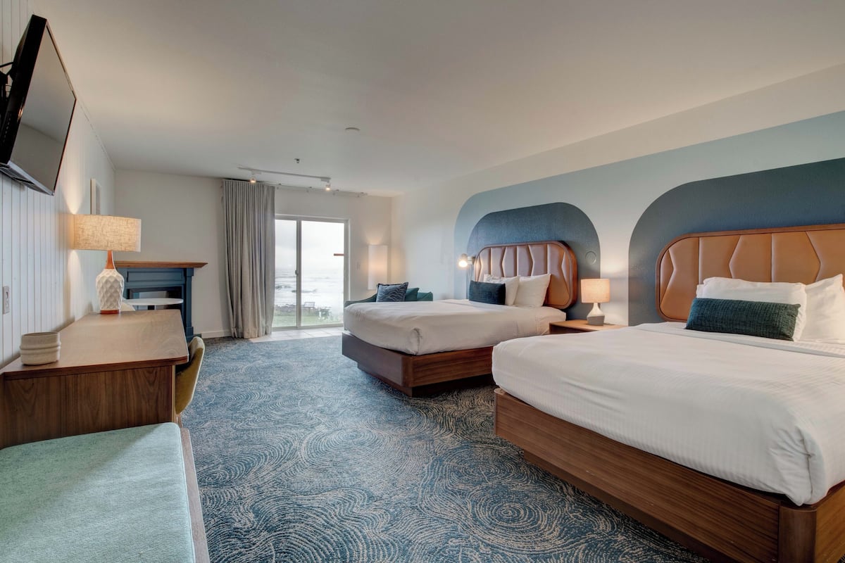 A hotel room with two beds, a desk, a TV, and a view of the outdoors.
