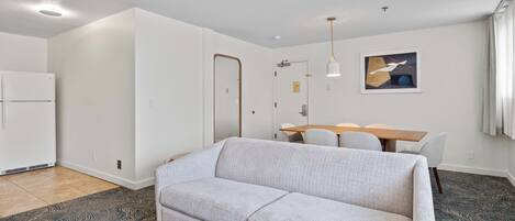 A modern living room with a sofa, a dining table with chairs, a kitchen area, and a ceiling light fixture.