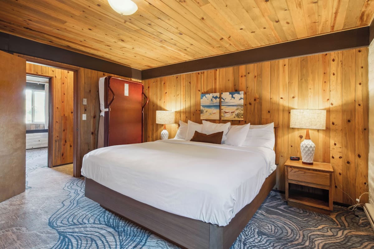 A wooden-paneled bedroom with a large bed, two bedside lamps, and a painting on the wall.