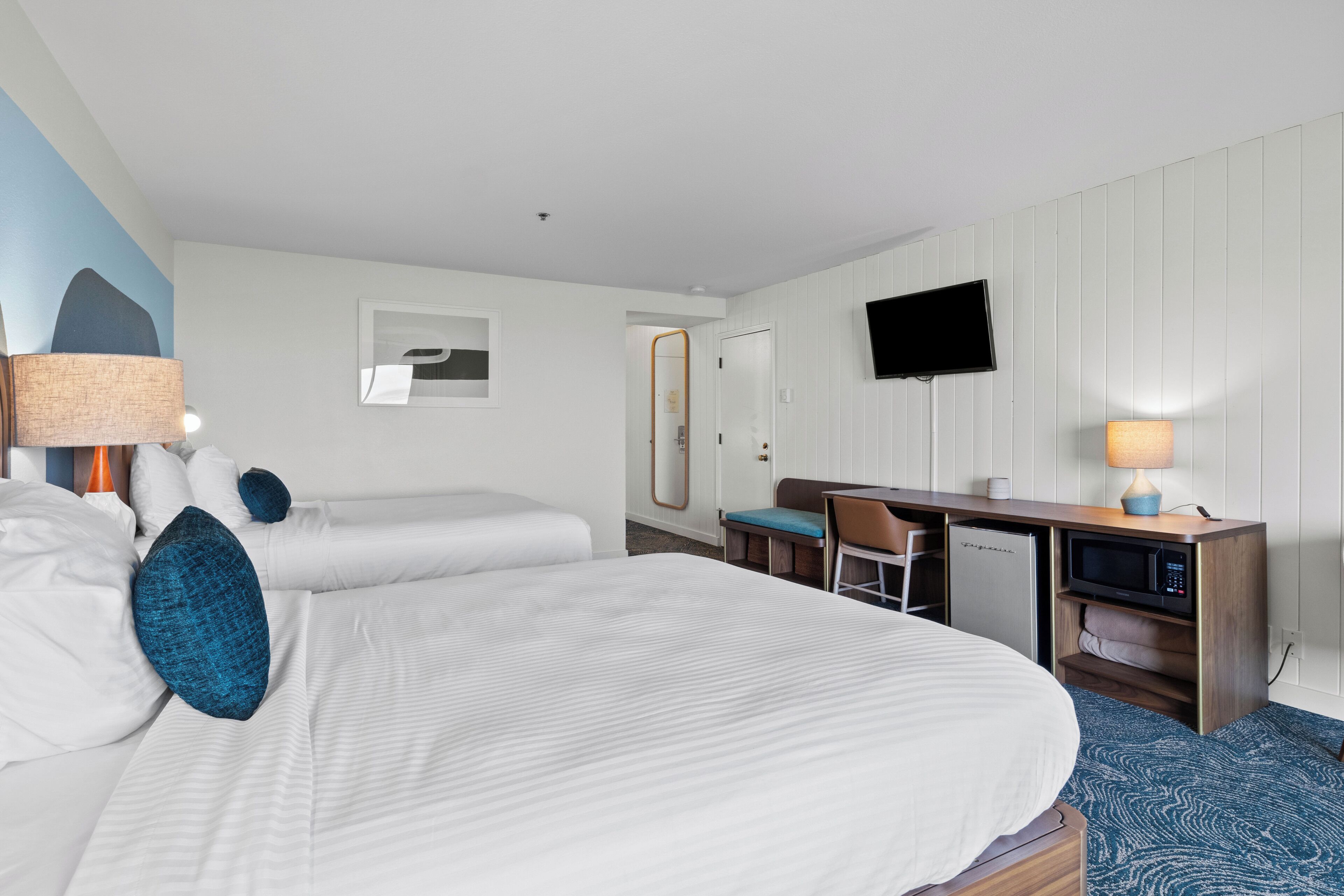 Una habitació d'hotel amb dos llits, un escriptori amb un ordinador, una televisió i un microones.