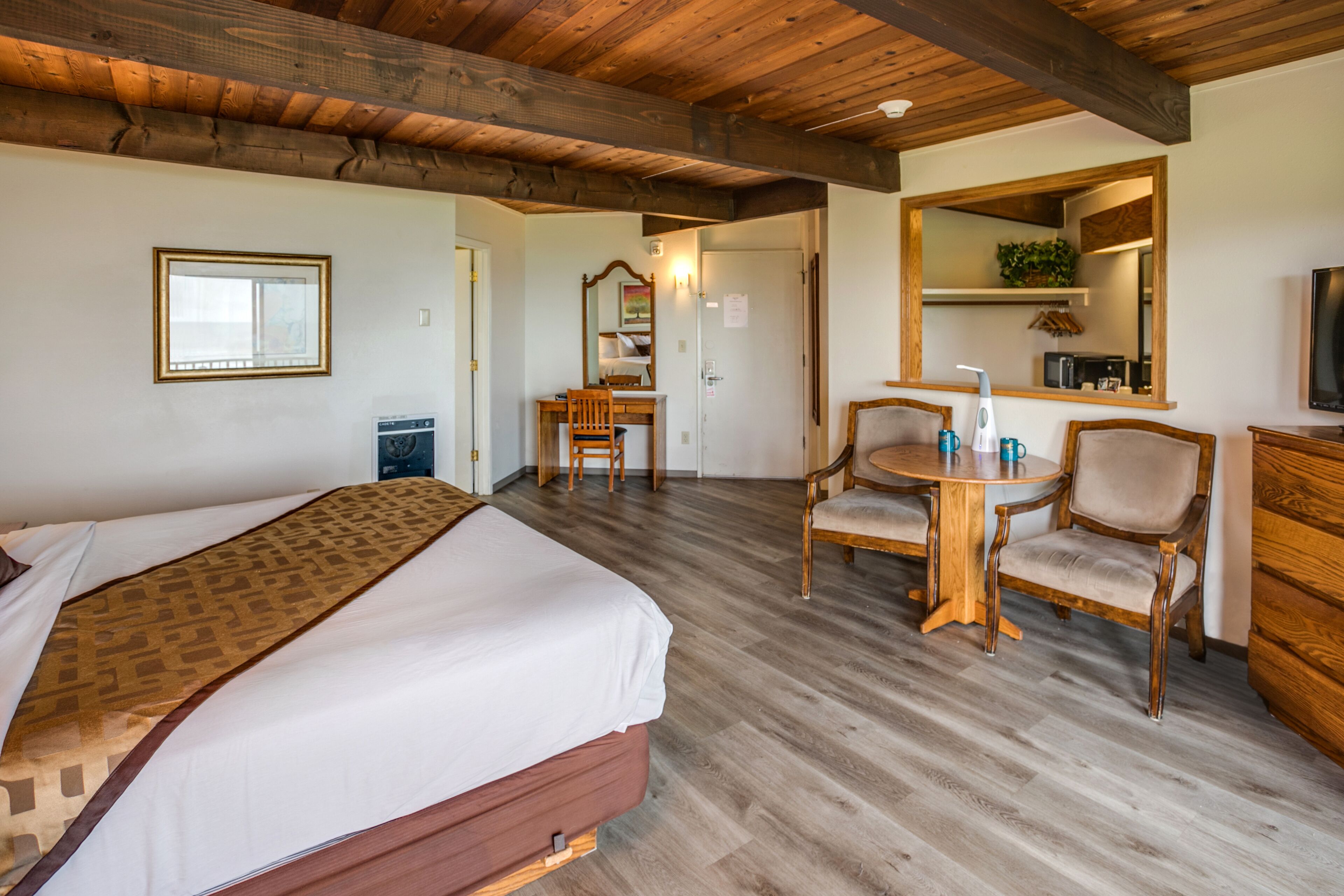 Une chambre d’hôtel comprenant un lit, un bureau avec des chaises, un miroir et un téléviseur.