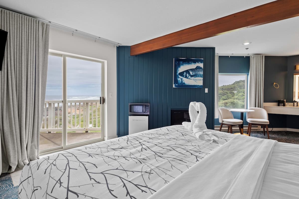 A hotel room with a large bed, a TV, a desk with chairs, and a view of the outdoors.