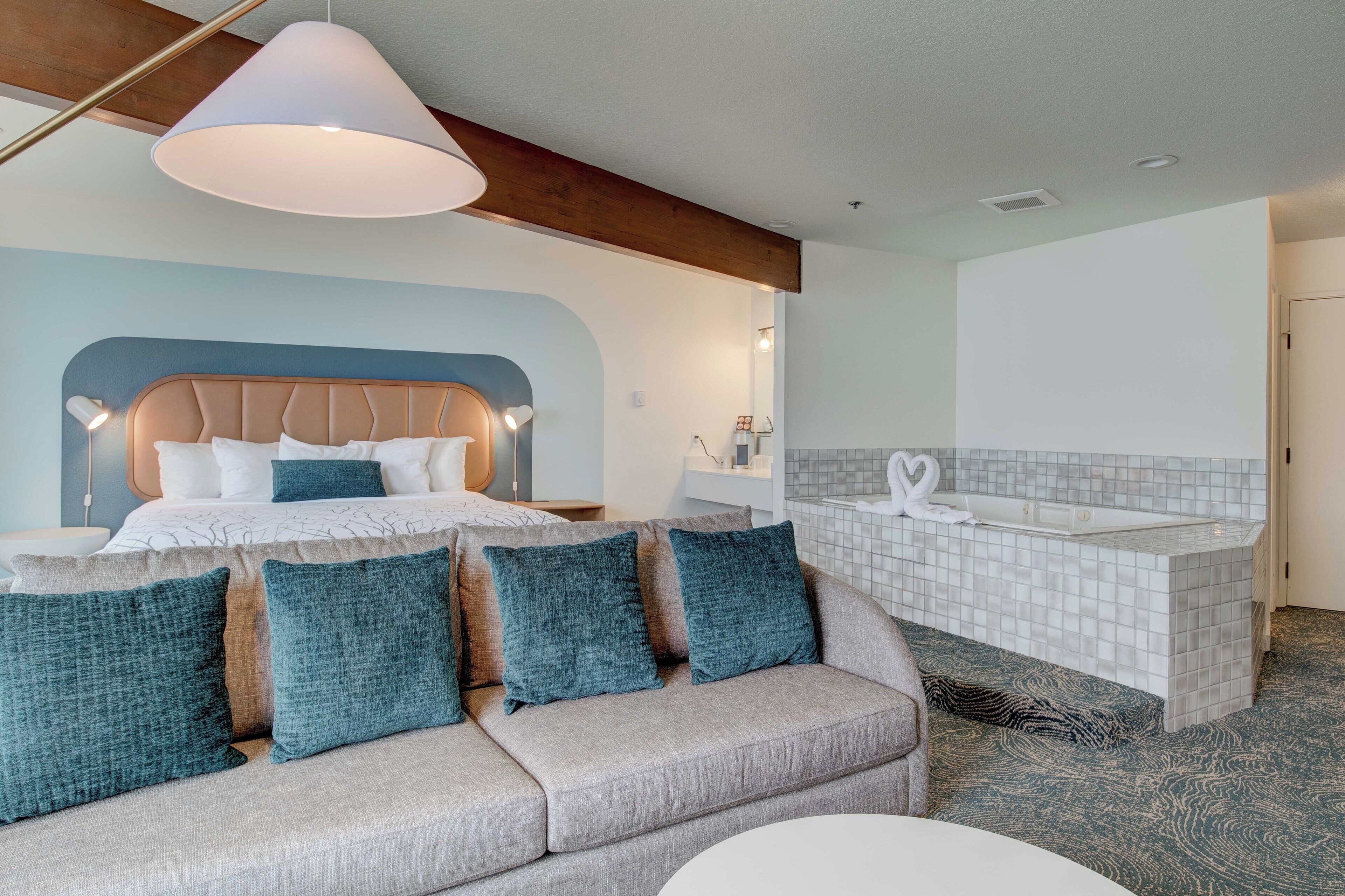 Une chambre d’hôtel moderne équipée d’un lit, d’un canapé, d’une salle de bain avec baignoire et d’une grande fenêtre.