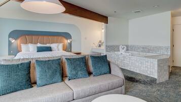 Una habitación de hotel moderna con cama, sofá, baño con bañera y un ventanal grande.