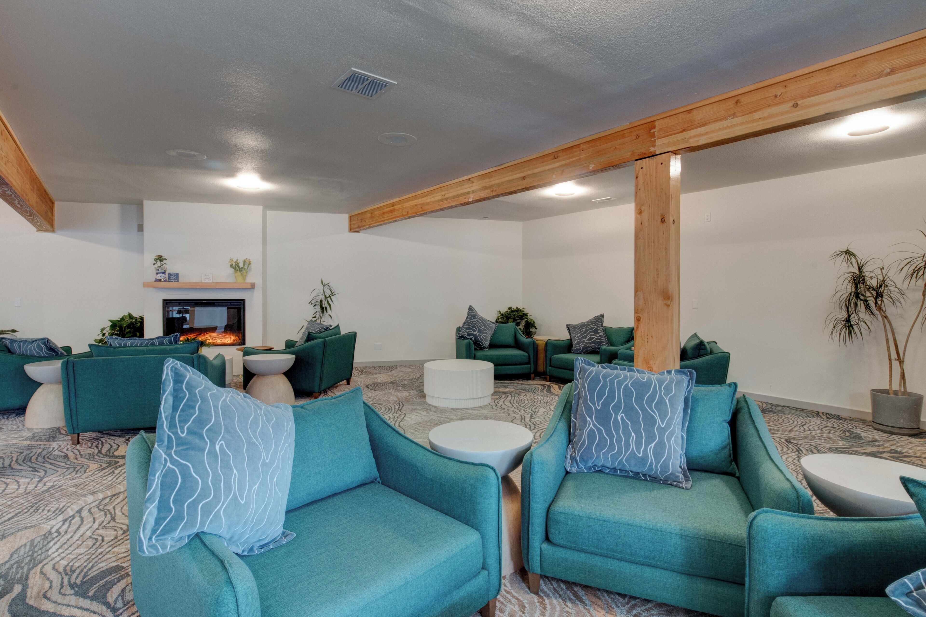 A spacious lounge area with teal sofas, white round coffee tables, and a fireplace.