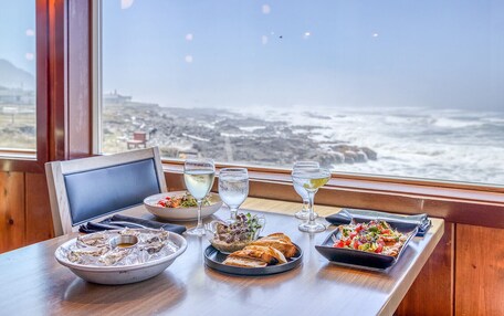 A table set with a variety of dishes and drinks, overlooking a coastal view.