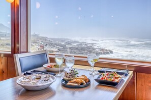A table set with a variety of dishes and drinks, overlooking a coastal view. - Adobe Resort (Yachats)
