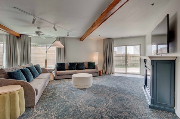 A spacious living room with a large sofa, a round coffee table, and a flat-screen TV mounted on the wall.