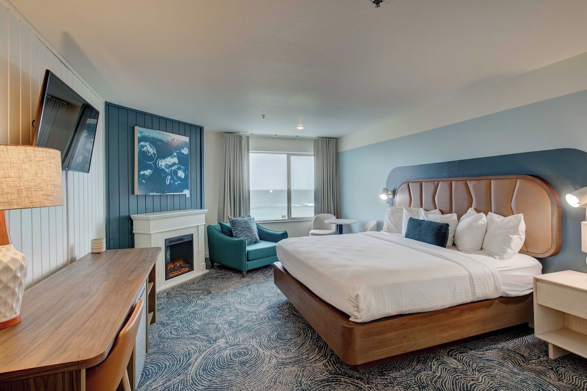 A hotel room with a bed, a desk, a chair, a fireplace, and a large window.