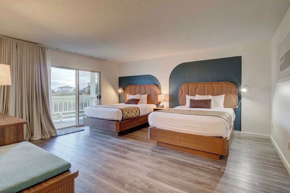 A hotel room with two beds, a sofa, and a balcony with curtains.