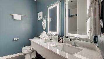 Un baño moderno con pared azul, dos lavabos, un inodoro y un espejo grande.