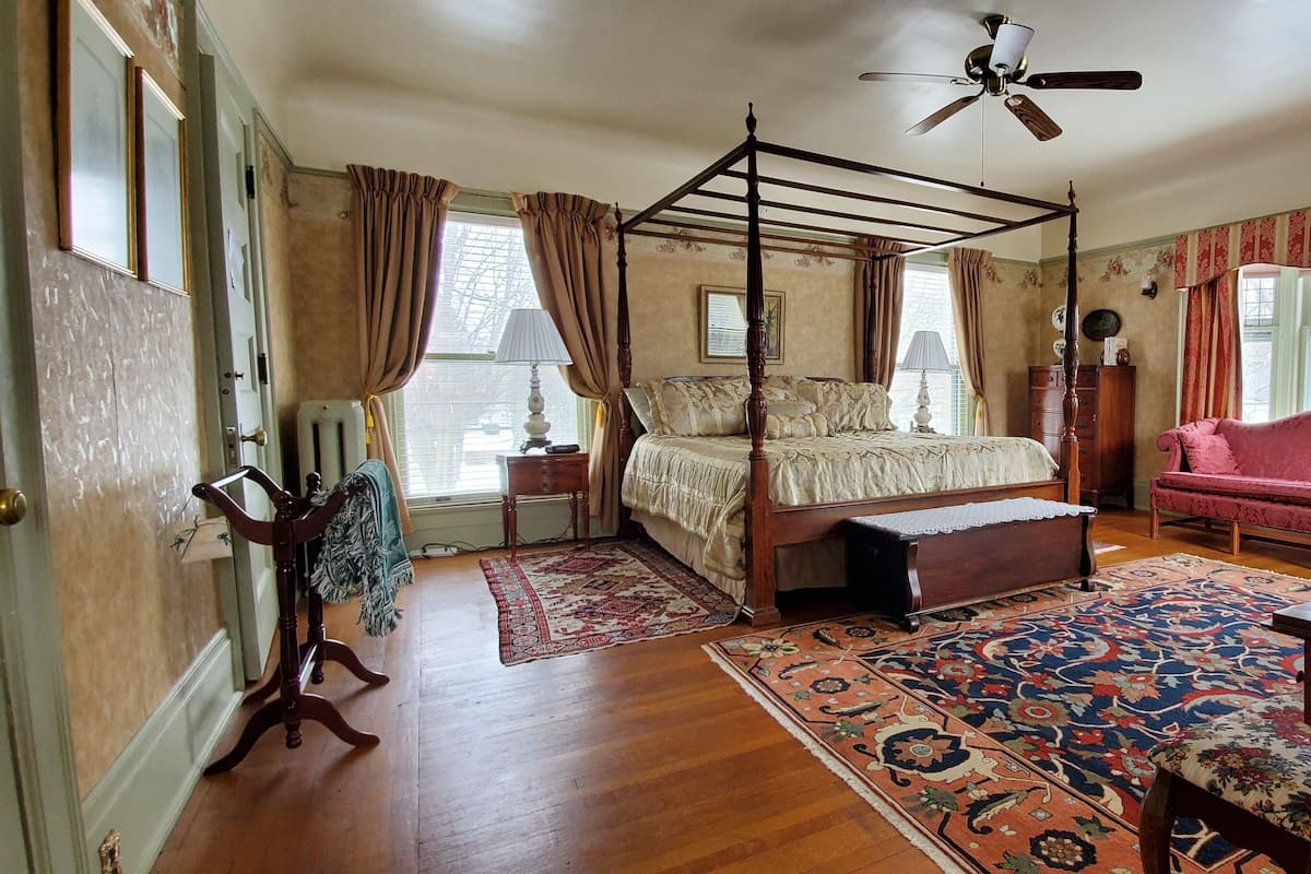 A bedroom with a four-poster bed, a red sofa, a wooden desk, and a large rug.